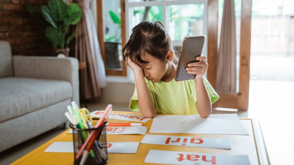 Niña con celular en mano frotándose los ojos