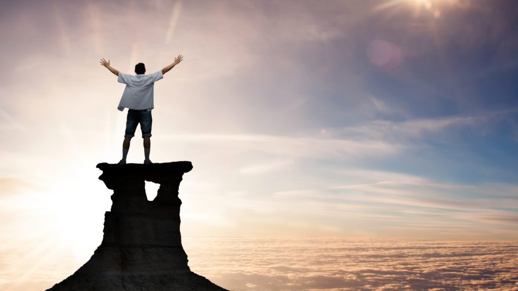 Hombre encima de una colina de piedra con brazos extendidos al cielo