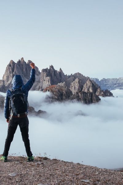 Hombre aventurero levantando una mano en lo alto de una montaña